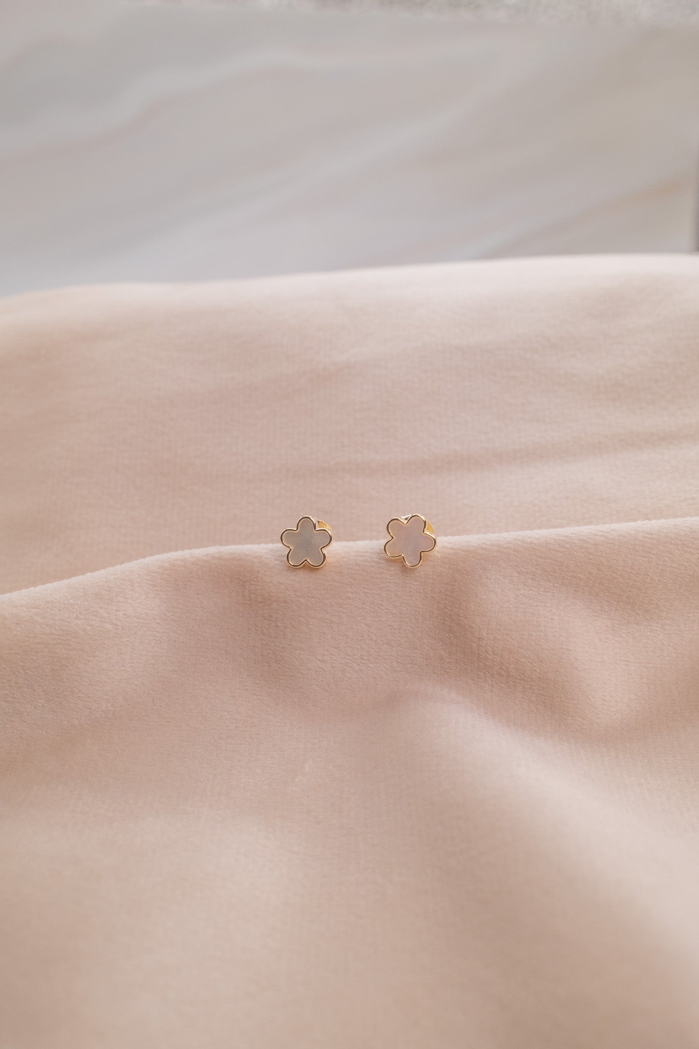Zamari delicate flower-shaped stud earrings from online dainty jewelry boutique on soft beige fabric