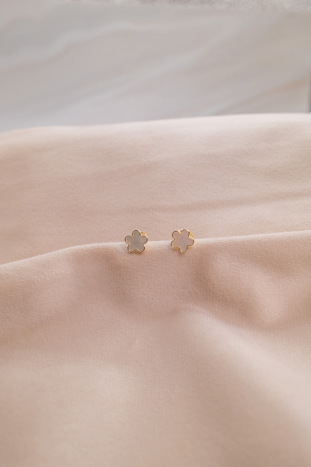 Zamari delicate flower-shaped stud earrings from online dainty jewelry boutique on soft beige fabric
