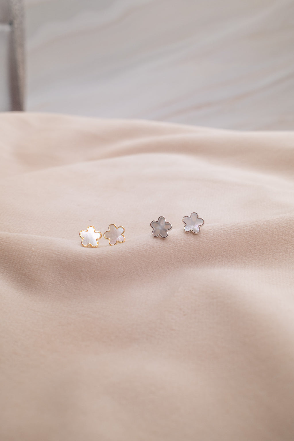 Zamari delicate flower-shaped earrings from an online dainty jewelry boutique on beige fabric