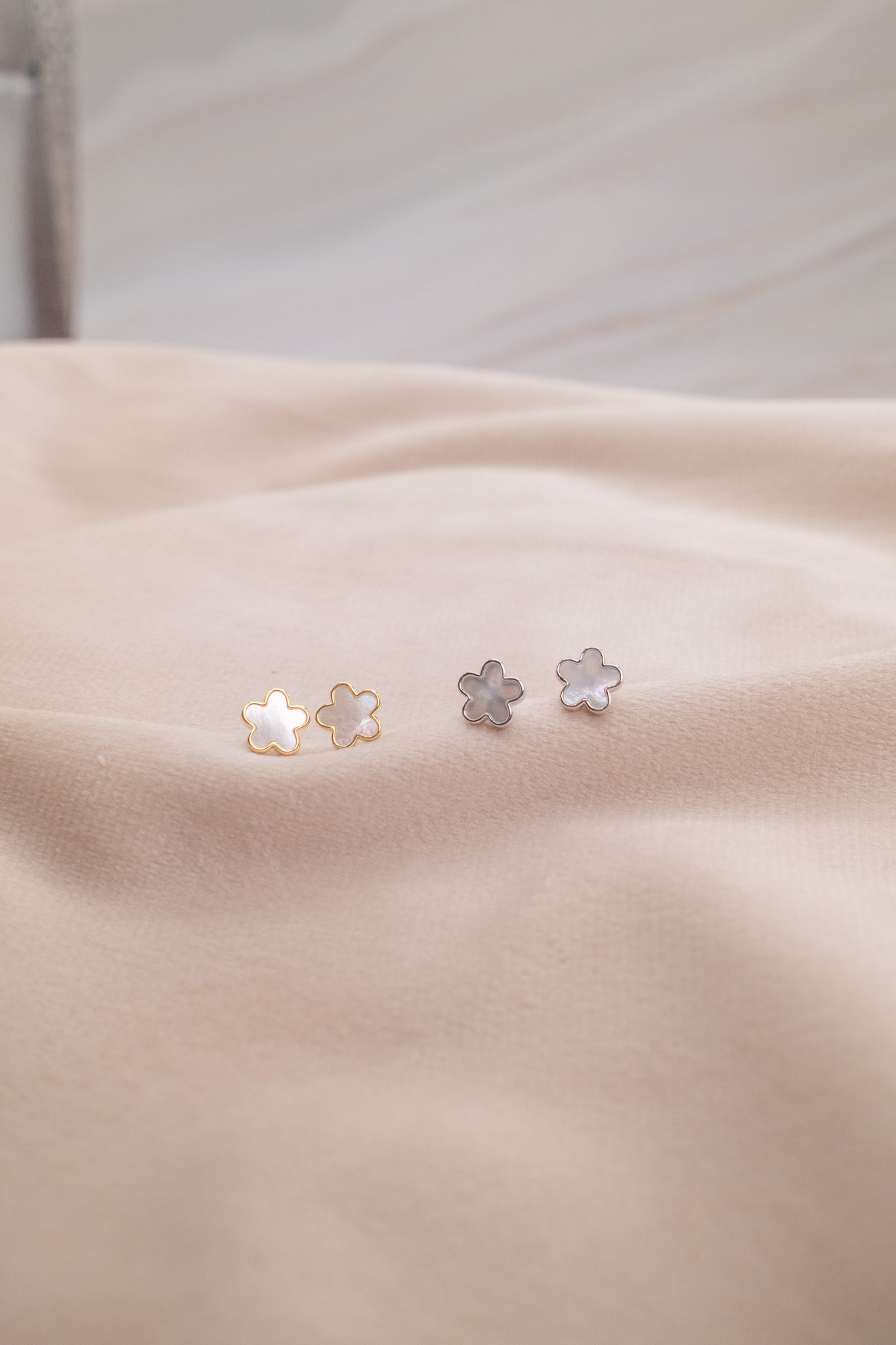 Zamari delicate flower-shaped earrings from an online dainty jewelry boutique on beige fabric