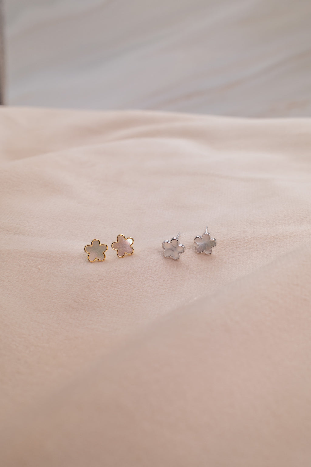 Zamari flower-shaped stud earrings in gold and silver displayed on beige fabric from online dainty jewelry boutique