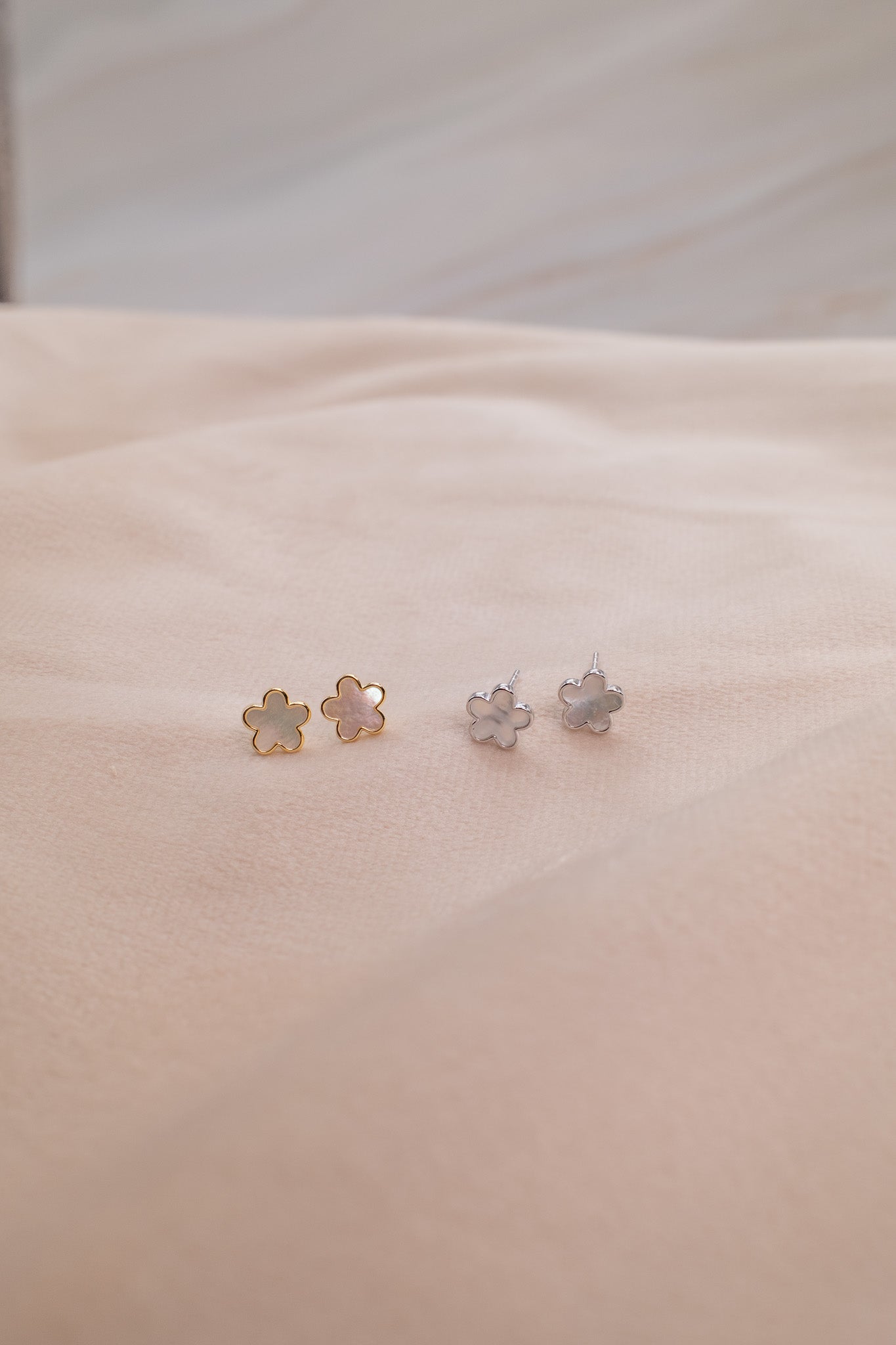 Zamari flower-shaped stud earrings in gold and silver displayed on beige fabric from online dainty jewelry boutique
