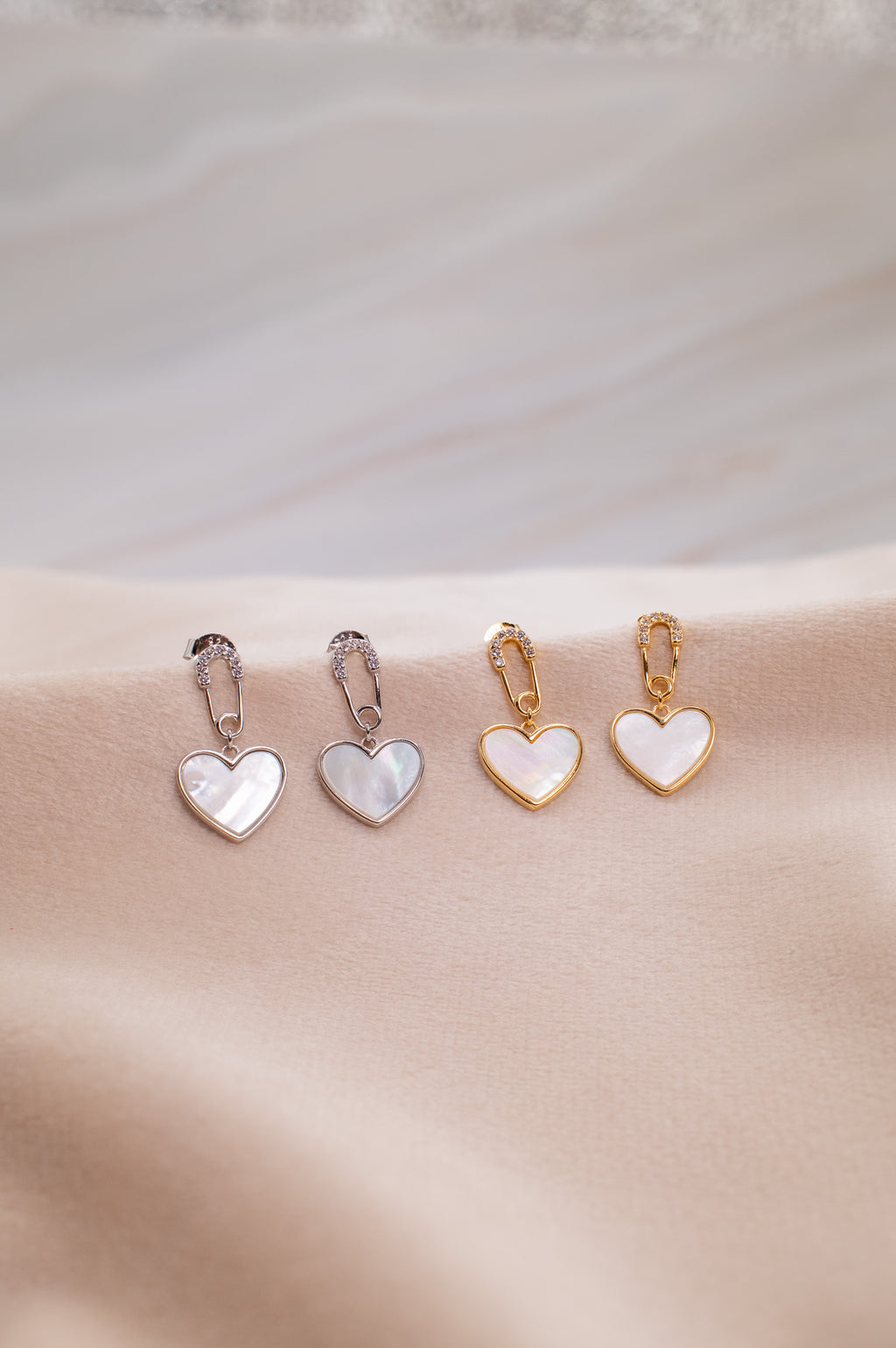 Zamari heart-shaped earrings in silver and gold displayed on beige fabric online dainty jewelry boutique