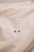Zamari blue eye stud earrings from online dainty jewelry boutique displayed on beige fabric