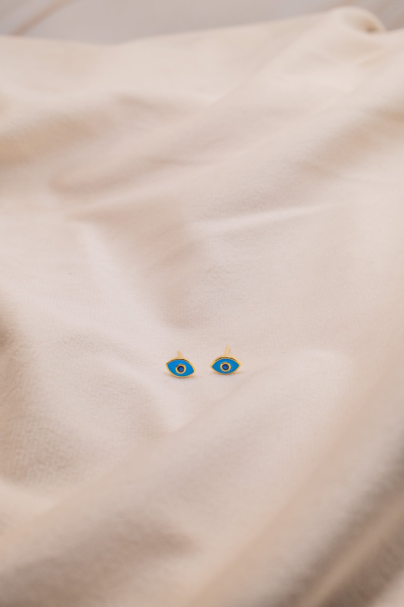 Zamari blue eye stud earrings from online dainty jewelry boutique displayed on beige fabric