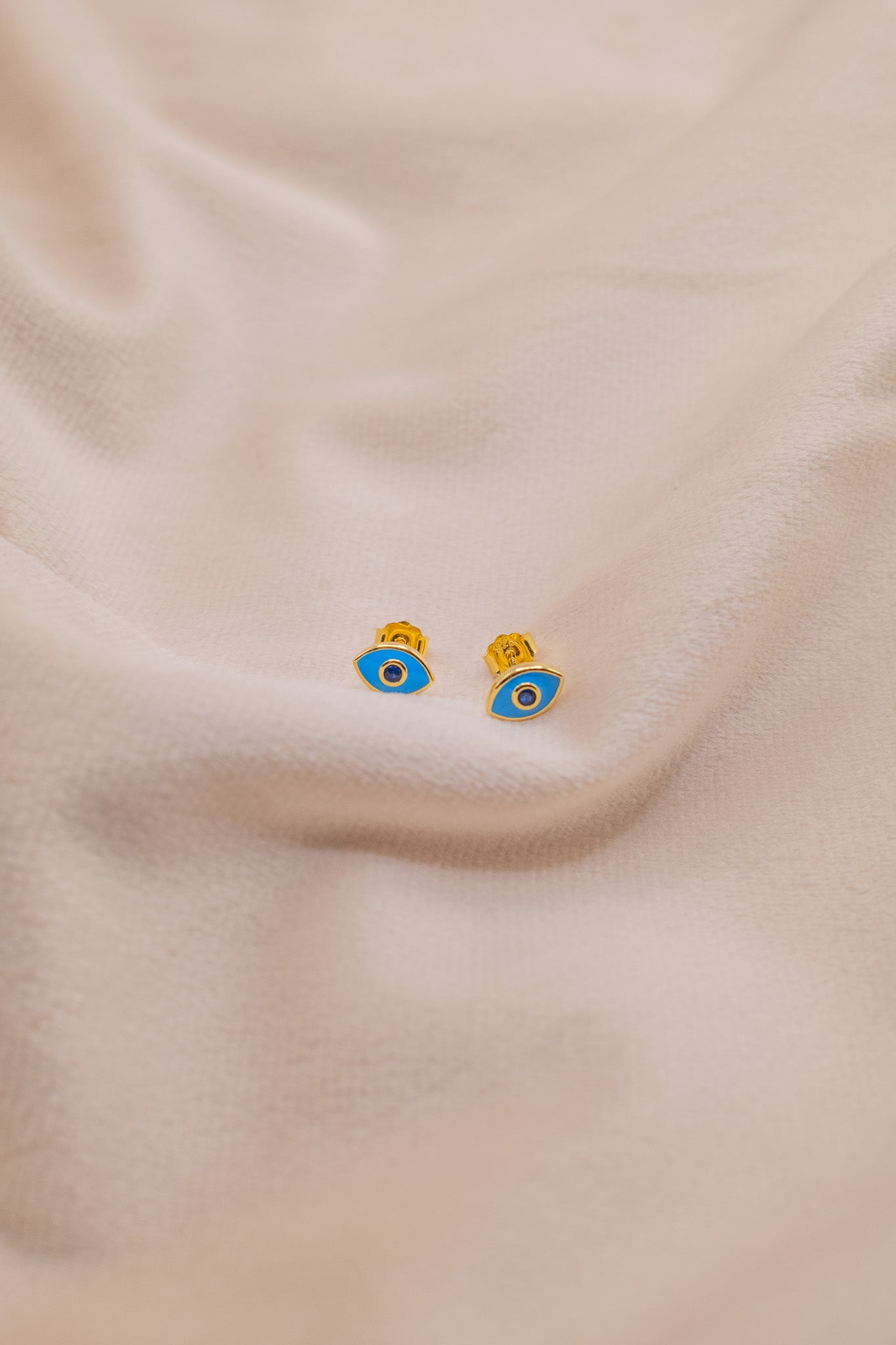 Zamari gold and blue eye-shaped earrings from an online dainty jewelry boutique on beige fabric