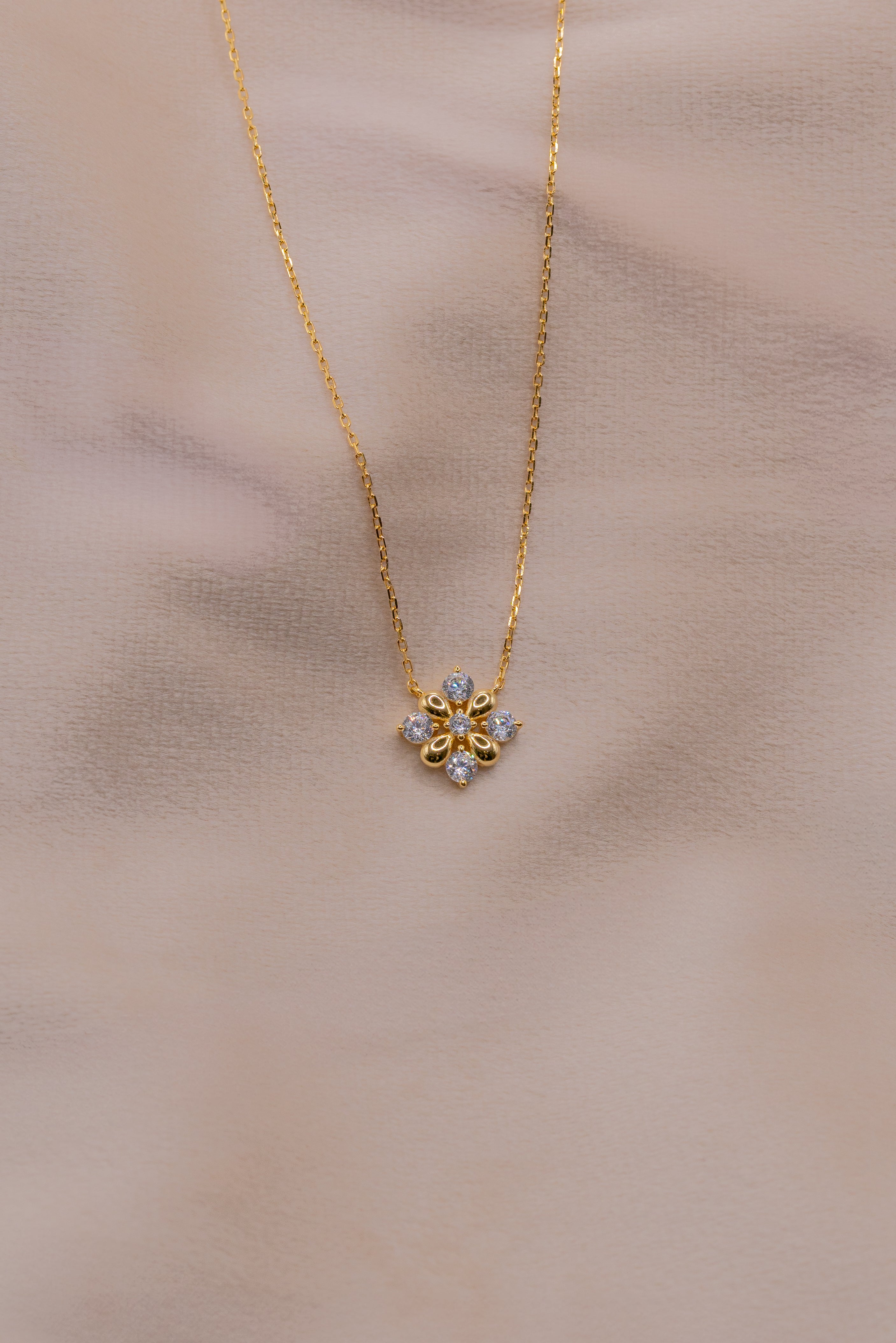 Zamari gold necklace with floral pendant from online dainty jewelry boutique on soft background