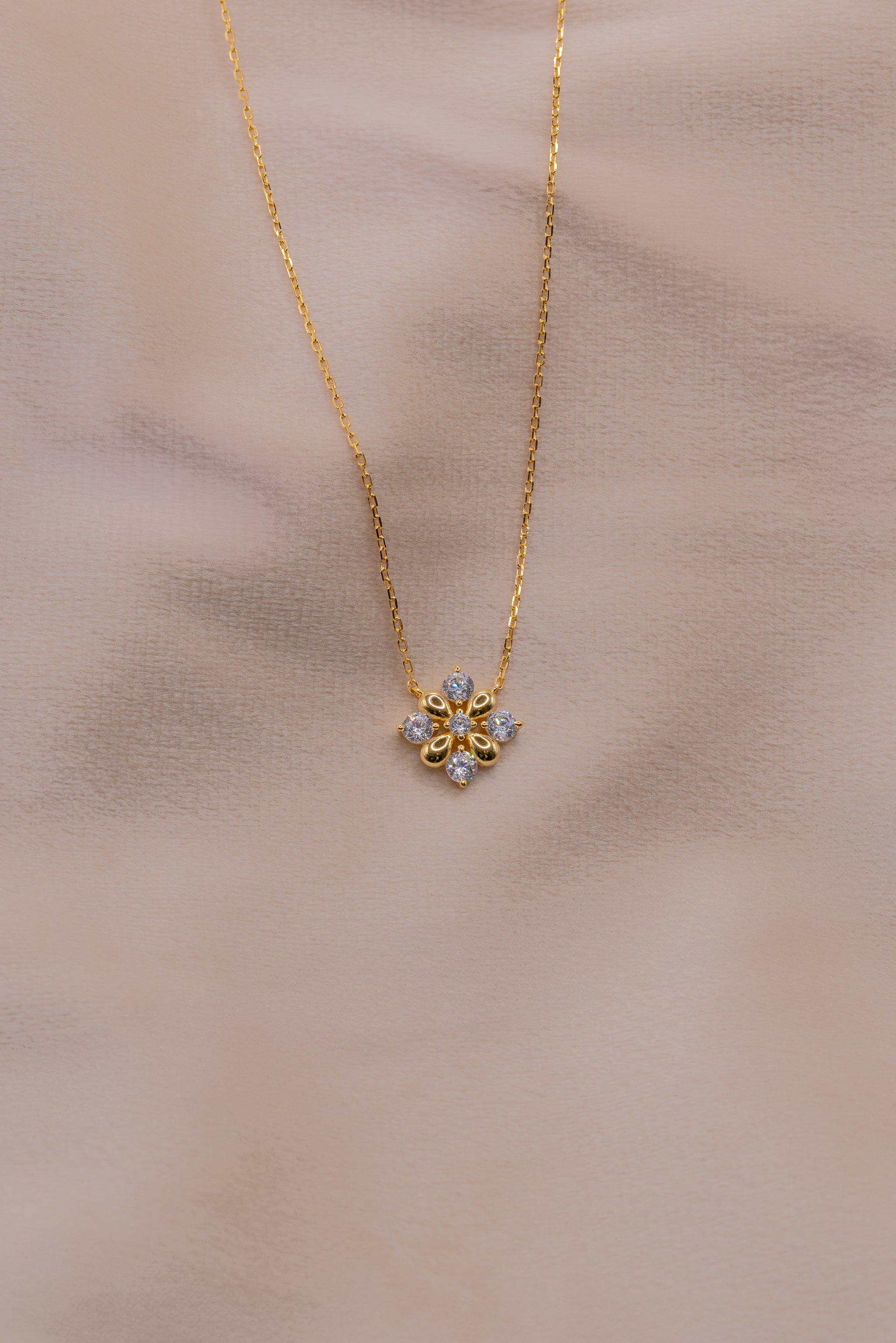Zamari gold necklace with floral pendant from online dainty jewelry boutique on soft background