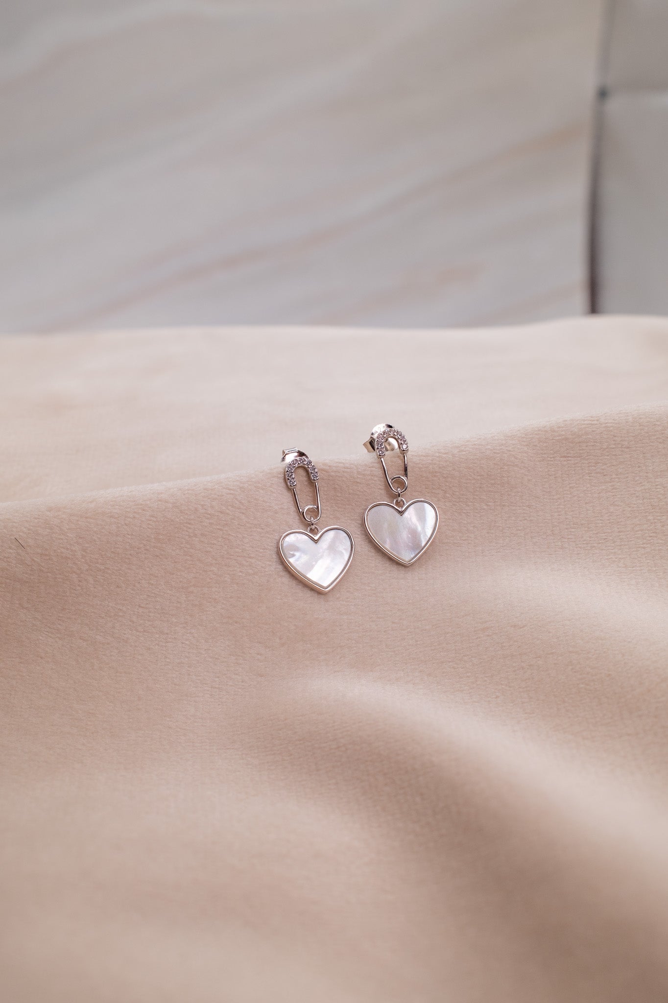 Zamari heart-shaped silver earrings displayed on beige fabric from online dainty jewelry boutique