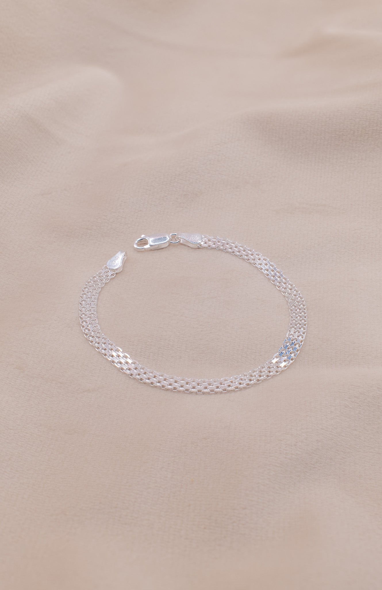 Zamari sterling silver jewelry bracelet with delicate chain design on beige fabric background