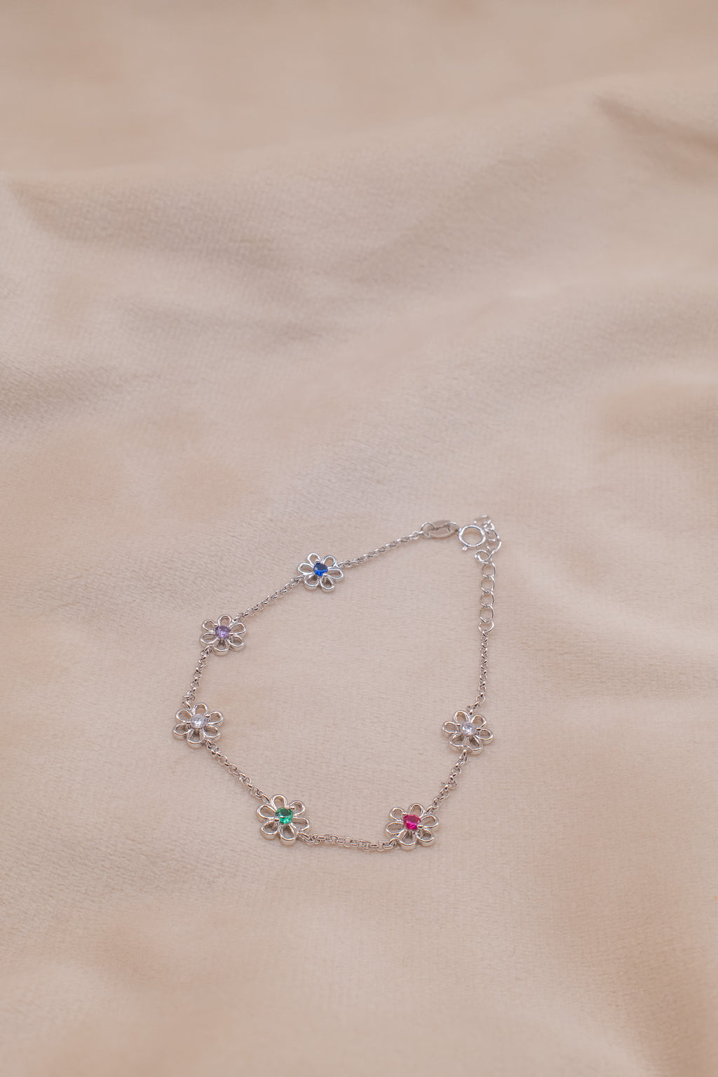Zamari delicate bracelet with colorful flower charms made of sterling silver jewelry on beige fabric