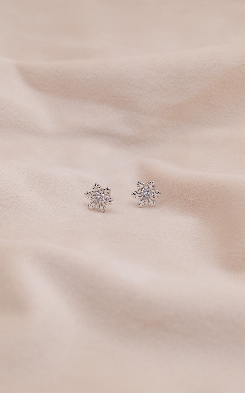 Zamari sterling silver jewelry snowflake stud earrings on soft beige fabric background