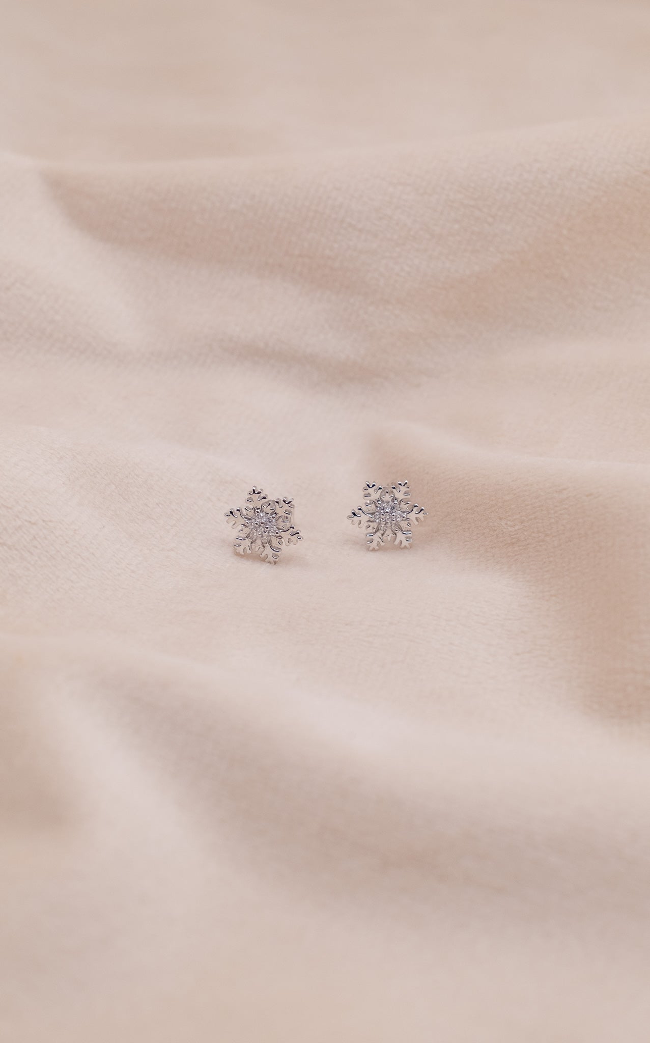 Zamari sterling silver jewelry snowflake stud earrings on soft beige fabric background