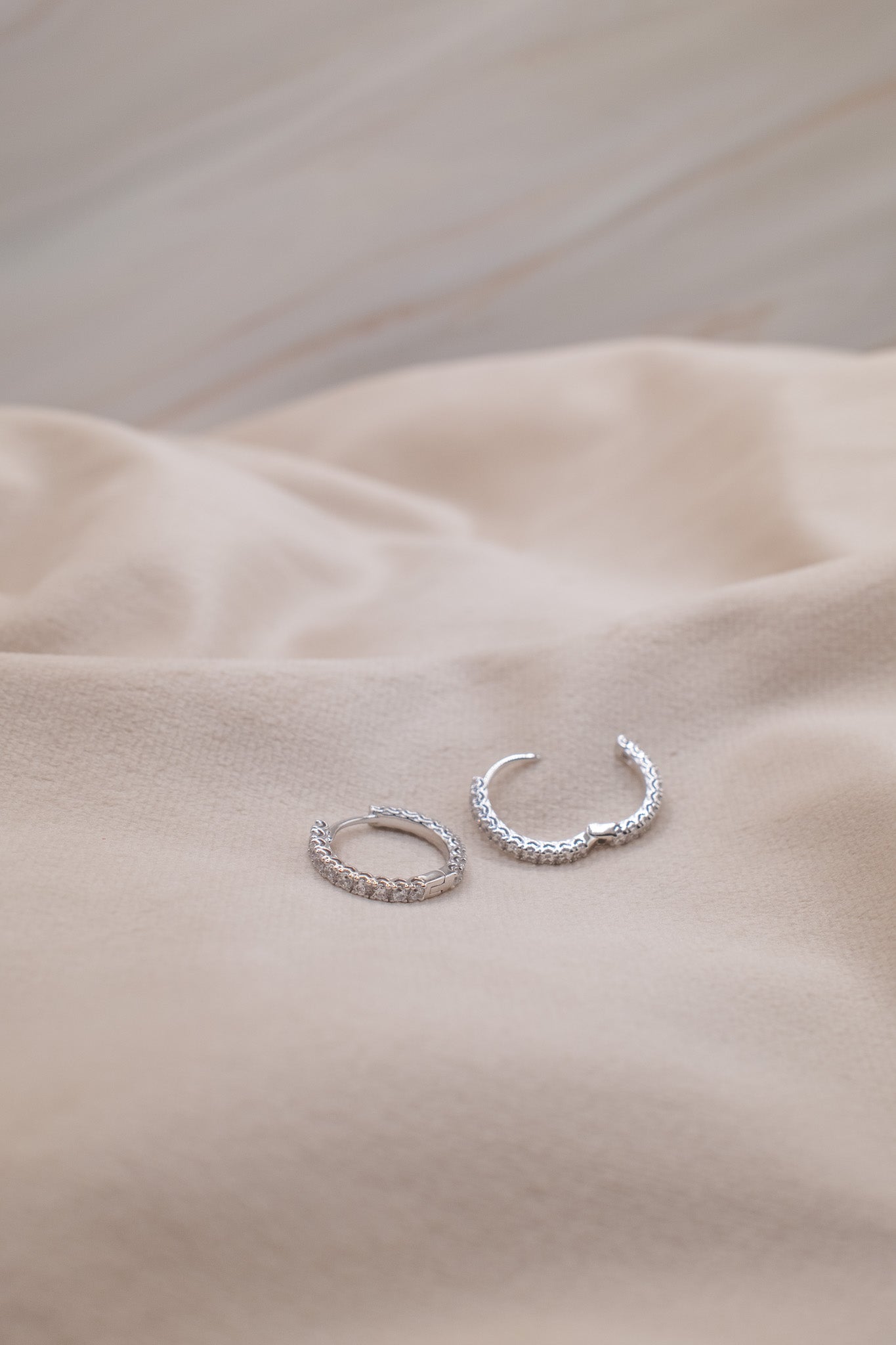 Zamari sterling silver jewelry hoop earrings with intricate design on beige fabric background